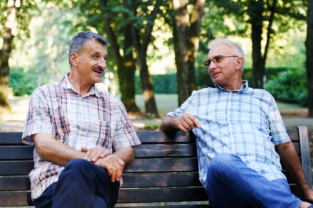 Two gentlemen sitting on a bench in a park.
